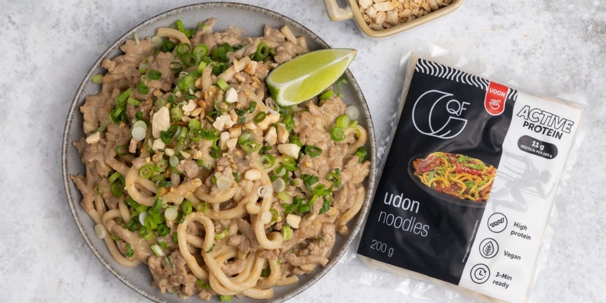 Talerz makaronu udon z mielonym indykiem w sosie orzechowym, obok limonka i opakowanie makaronu Udon QF Active